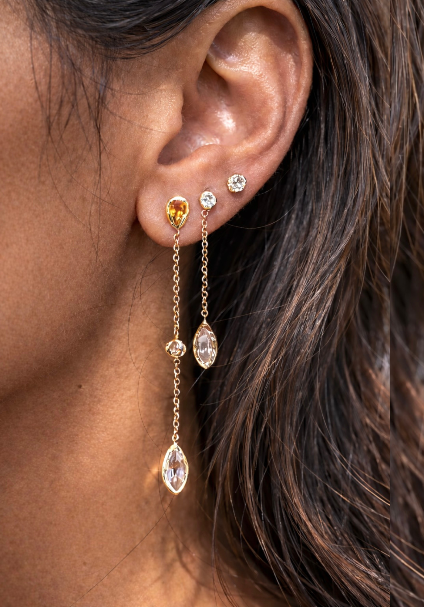 Close-up of an ear wearing a set of gold earrings with gemstones.