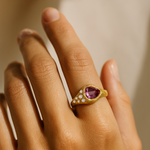 A gold ring featuring a pink drop-shaped tourmaline centerpiece with rose-cut diamond accents.

